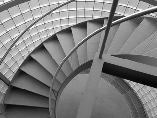 Grey spiral staircase with glass wall and stone steps and metal railing