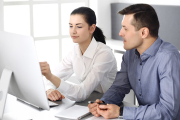 Obraz premium Cheerful smiling businessman and woman working with computer in modern office. Headshot at meeting or workplace. Teamwork, partnership and business concept 