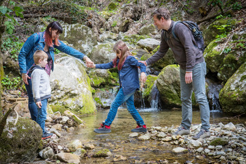 mom and dad help children cross the mountain stream