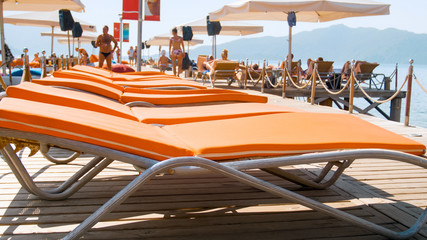 Closeup image of straight rows of sun beds on wooden pier at bright sunny day