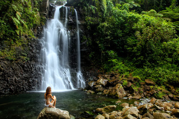 Young woman in bikini sitting by Middle Tavoro Waterfalls in Bouma National Heritage Park, Taveuni...