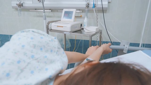 Woman lying in the hospital room, holding the handrail. The arm includes a catheter around the sensors for the heart rate and pressure. The woman is preparing for childbirth and surgery. 4K