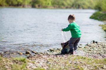 Save environment concept, a little boy collecting garbage and plastic bottles on the beach to dumped into the trash.