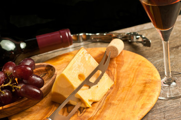 Fototapeta na wymiar Top view, close distance of a round, rare wood plate with a wedge of french cheese, cheese knife and a wood bowl of red grapes with a corkscrew and cork, neck unopened bottle, red wine