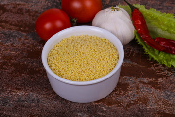 Raw couscous in the bowl served salad leaves, tomato and pepper