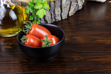 tomatoes in a black cup, olive oil and parsley on dark wood table 