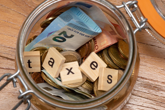 Pi&egrave;ces et billets en euros dans un bocal avec le mot "taxes" compos&eacute; avec des lettres en bois