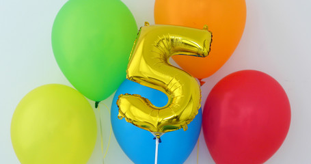 Gold foil number 5 celebration balloon on a color background