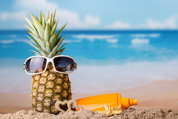 Concept of rest. Pineapple in sunglasses in sand and cream for sun protection