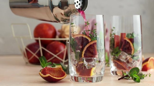 Pouring red orange juice in a large glass or blood orange sparkling vodka cocktail or aperitif with campari, slow motion full hd video
