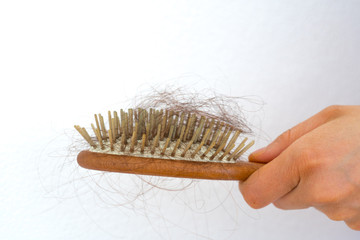 woman holding wooden hair brush full of hair that has fallen out