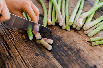 female cook cutting and preparing green asparagus with a sharp knife
