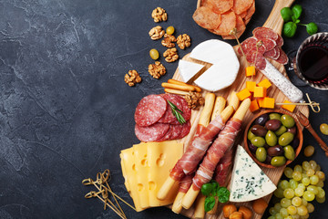 Italian appetizers or antipasto set with gourmet food on black kitchen table top view. Mixed delicatessen of cheese and meat snacks with red wine.