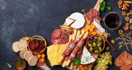 Italian appetizers or antipasto set with gourmet food on black table top view. Mixed delicatessen of cheese and meat snacks with red wine.