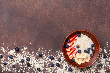 Obraz na płótnie Canvas Bowl of oatmeal porridge with strawberry, blueberry and banana on brown table top view. Healthy breakfast.