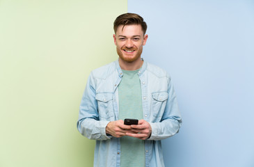 Redhead man over colorful background sending a message with the mobile