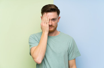 Redhead man over colorful background covering a eye by hand