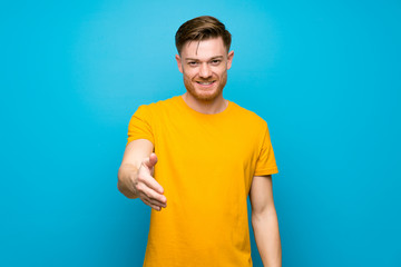Redhead man over blue wall shaking hands for closing a good deal
