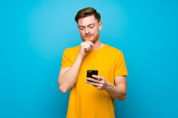 Redhead man over blue wall thinking and sending a message