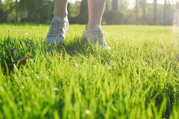 Woman walks in white sneakers in green spring  park.