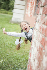 Portrait of a beautiful young schoolgirl peeking from behind a brick wall