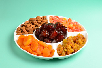 Mix of dried fruits and nuts on a white plate. Apricot, almond, raisin, dates fruit. On a green background. Space for text or design.