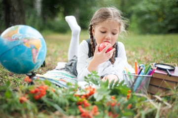 Portrait of a schoolgirl in the park on the grass with a globe, books and an apple