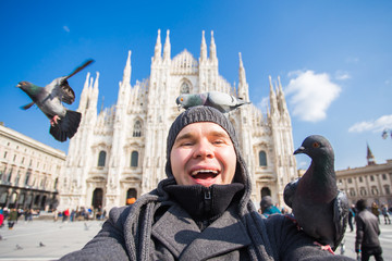 Winter travel, vacations and birds concept - Young funny man taking selfie with pigeons near Milan Cathedral Duomo di Milano, Italy.