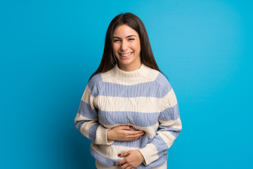 Young woman over blue wall smiling a lot while putting hands on chest