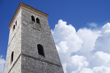 Fototapeta na wymiar Old stone bell tower, a view from below, with a background of blue sky and snowy white clouds