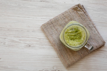 Green celery smoothie in a glass jar over white wooden surface. Overhead, flat lay, from above. Copy space.
