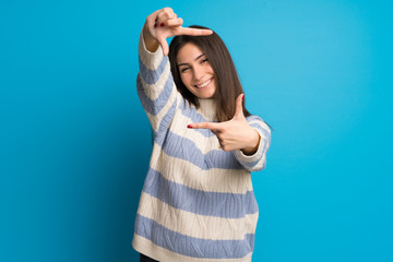 Young woman over blue wall focusing face. Framing symbol