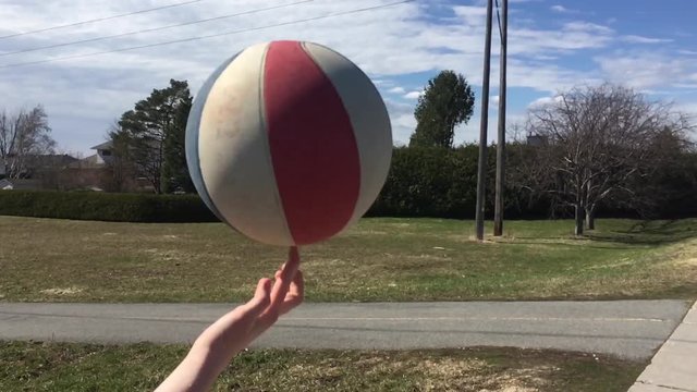 Girl spins ball on finger in slow motion at sunset.
