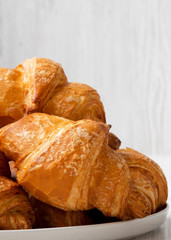 Freshly baked croissants on a round plate over white wooden surface, side view. Close-up.