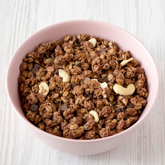 Homemade chocolate granola with nuts in a pink bowl over white wooden surface, low angle view. Closeup.