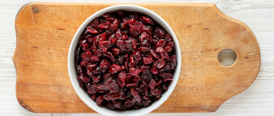Dry organic cranberries in a gray bowl on rustic board over white wooden background, top view. Overhead, from above, flat lay.