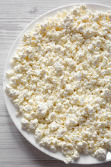 Homemade cottage cheese on a white plate, top view. Flat lay, overhead, from above. Close-up.