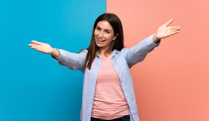 Young woman over pink and blue wall presenting and inviting to come with hand