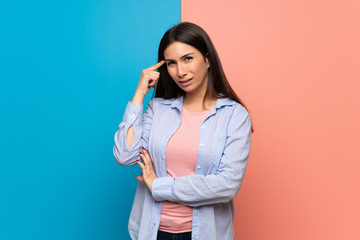 Young woman over pink and blue wall making the gesture of madness putting finger on the head