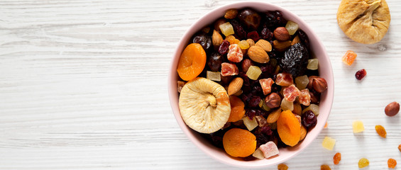 Dried fruits and nuts in a pink bowl over white wooden background, top view. Overhead, from above, flat lay. Copy space.