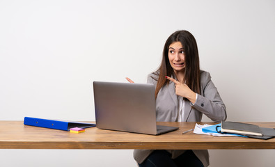 Business woman in a office frightened and pointing to the side