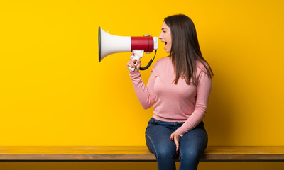 Young woman sitting on table shouting through a megaphone