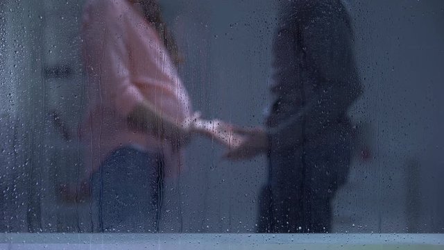 Couple quarrelling, man hitting pregnant woman behind rainy window, aggression