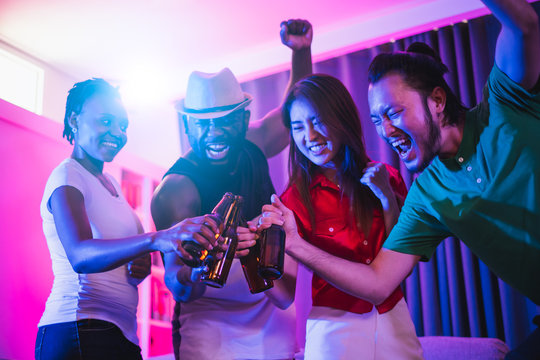 Group Of People Enjoy Night Glow Disco Party Singing Songs, Dancing, Drinking Alcohol At Private Home By Blue And Pink Light