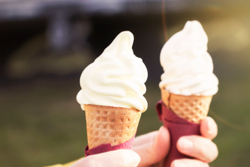 Woman's hands holding melting ice cream waffle cone in hands on summer light nature background