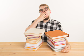 People, exam and education concept - Exhausted and tired student dressed in plaid shirt sitting at the wooden table with many books