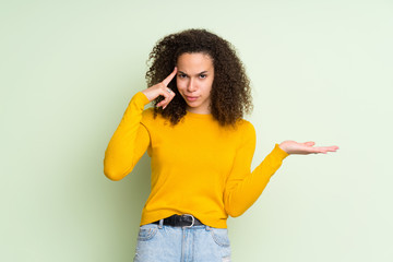 Dominican woman over isolated green background making the gesture of madness putting finger on the...