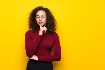 Dominican woman with turtleneck sweater showing a sign of silence gesture putting finger in mouth