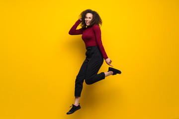Fototapeta na wymiar Dominican woman with curly hair jumping over isolated yellow wall