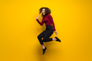 Fototapeta na wymiar Dominican woman with curly hair jumping over isolated yellow wall